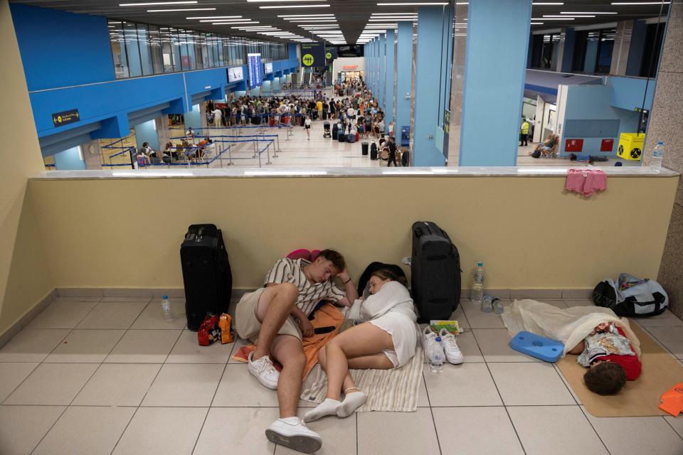 Tourists rest as they wait in the airport’s departure hall as evacuations are underway due to wildfires, on the Greek island of Rhodes (Reuters)