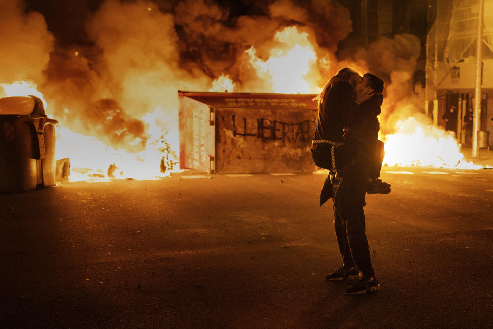 A couple kiss in front of a barricade set by demonstrators during clashes with police following a protest condemning the arrest of rap singer Pablo Hasél in Barcelona, Spain, Thursday, Feb. 18, 2021. Protests over the imprisonment of a rapper convicted for insulting the Spanish monarchy and praising terrorist violence have morphed for the third night in a row into rioting. Pablo Hasél began this week to serve a 9-month sentence in a northeastern prison. (AP Photo/Emilio Morenatti)