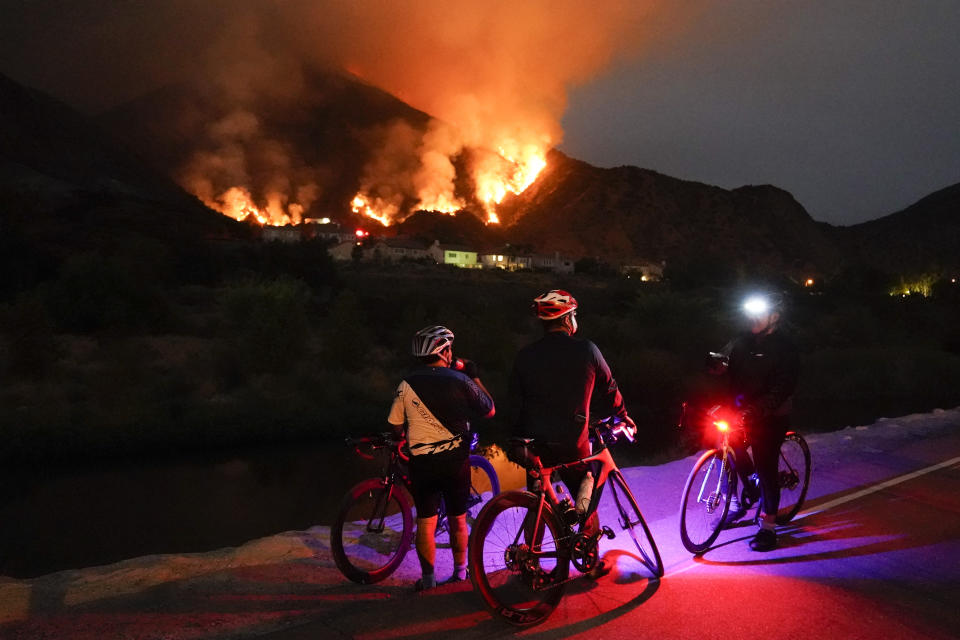 Cyclists rest along a trail as the Ranch Fire burns, Thursday, Aug. 13, 2020, in Azusa, Calif. Heat wave conditions were making difficult work for fire crews battling brush fires and wildfires across Southern California. (AP Photo/Marcio Jose Sanchez)