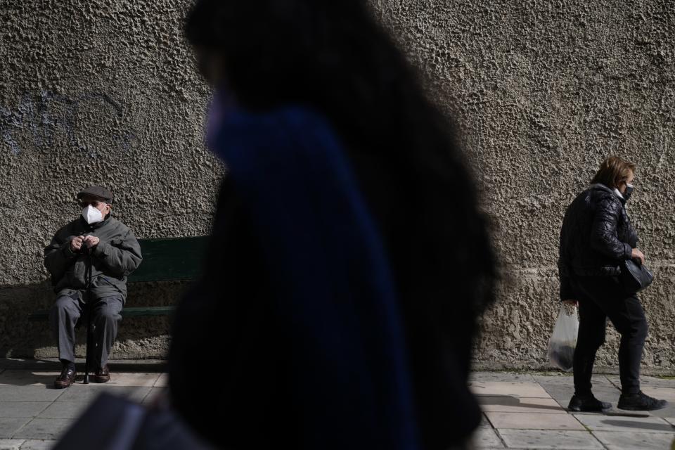 A man wearing a face mask to curb the spread of coronavirus, sits on a bench as pedestrians walk outside Evangelismos hospital in Athens, Greece, Monday, Jan. 17, 2022. Greece has imposed a vaccination mandate for people over age 60, as coverage remains below the European Union average and while a recent spike in infections has sustained pressure on hospitals. (AP Photo/Thanassis Stavrakis)