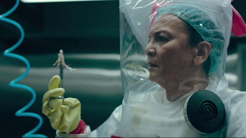 A woman in a hazmat suit holds up infectious fungal tendrils with a pair of tongs.