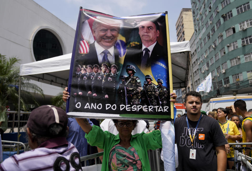 A supporter of Brazilian President Jair Bolsonaro holds a poster showing Bolsonaro and former U.S. President Donald Trump that reads in Portuguese "The year of the awakening" during Bolsonaro's campaign rally for reelection in Duque de Caxias, Rio de Janeiro state, Brazil, Friday, Oct. 14, 2022. The presidential run-off election is set for Oct. 30. (AP Photo/Silvia Izquierdo)