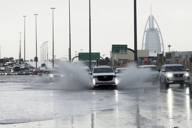 An SUV splashes through standing water on a road with the Burj Al Arab luxury hotel seen in the background in Dubai, United Arab Emirates.