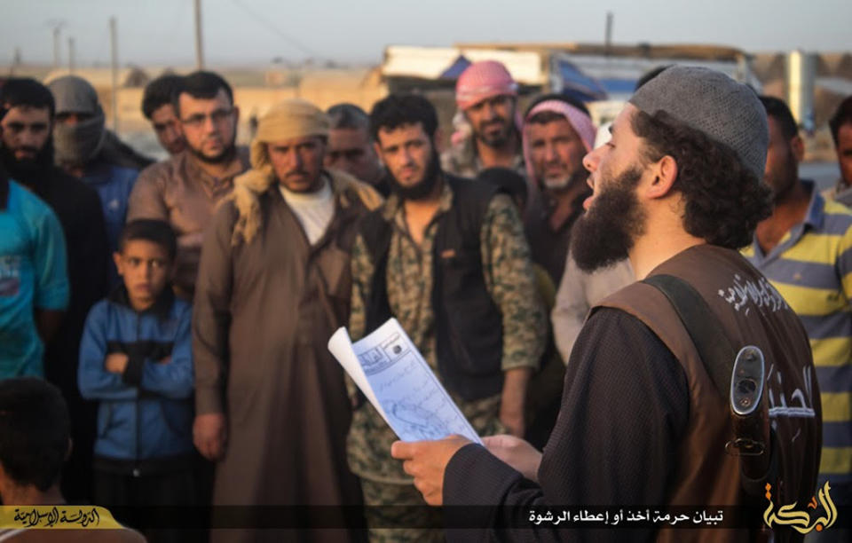 In this file photo released on May 14, 2015, by a militant website, which has been verified and is consistent with other AP reporting, a member of the Islamic State group's vice police known as Hisba, right, reads out to Syrian citizens, background, a verdict handed down by an Islamic court sentencing many they accused of adultery to lashing, in Raqqa city, Syria. (Militant website via AP, File)