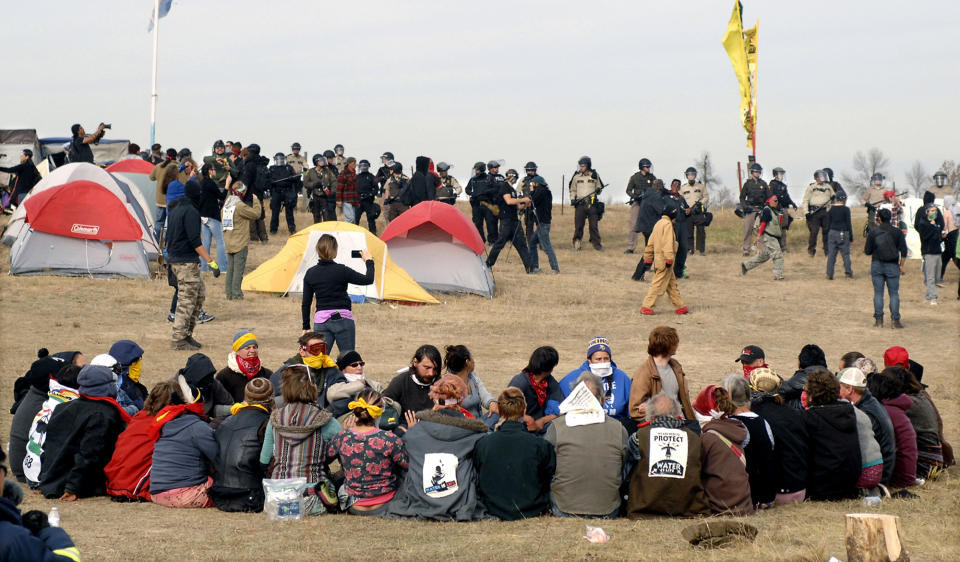 FILE - In this Oct. 27, 2016, file photo, Dakota Access Pipeline protesters sit in a prayer circle at the Front Line Camp as a line of law enforcement officers make their way across the camp to remove the protesters and relocate to the overflow camp a few miles to the south on Highway 1806 in Morton County, N.D. President Joe Biden has committed to regular and meaningful consultation with tribal nations on federal policies and projects that affect them. The Interior Department has scheduled a series of talks with tribes in March 2021 on health, the economy, racial justice and the environment. (Mike McCleary/The Bismarck Tribune via AP, File)
