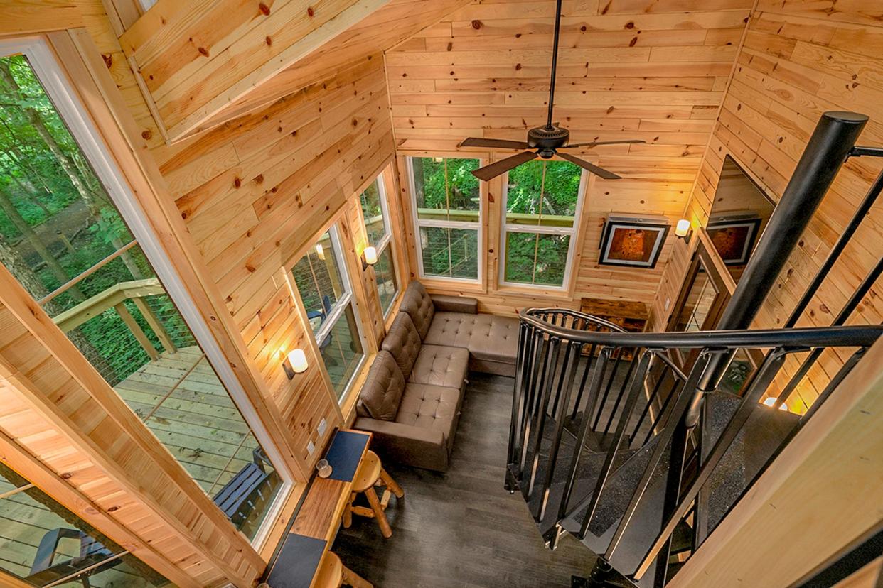 The treehouse has a patio for scenic viewing, with a primary bedroom, living room area, kitchen, restroom, shower, washer and dryer inside. Up the spiral staircase is a bunk bed and flat screen TV.