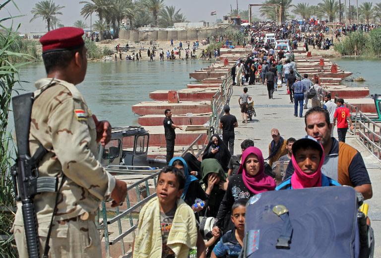 Iraqi security forces stand guard as residents from the city of Ramadi, who fled from Islamic State (IS) militants, wait to cross a bridge into Baghdad, on May 20, 2015