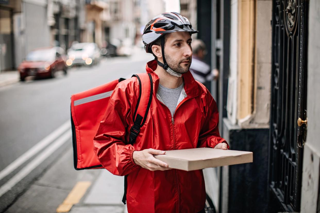 Delivery boy in red uniform holding pizza box in front of door, making a home delivery