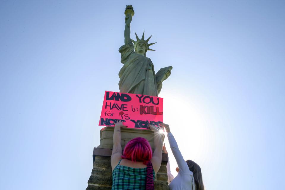 Nora Cole, left, and Zee Lauer, both sophomores, place a sign reading “Land you have to kill for is not yours” on the Statue of Liberty Friday, May 3, 2024 at the City High school protest over the Israel-Hamas war in Iowa City, Iowa.