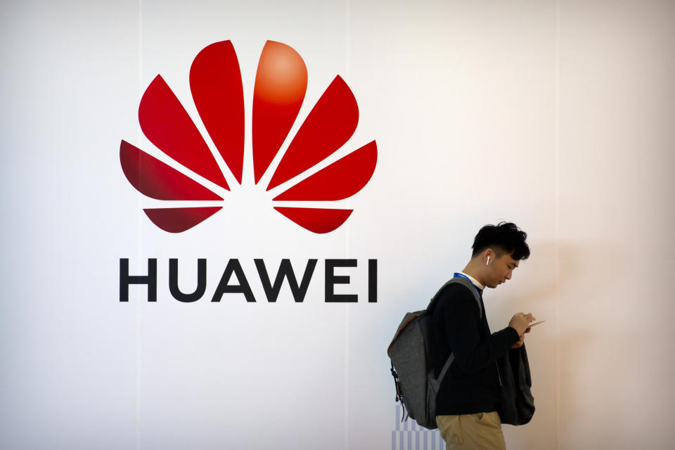 FILE - In this Oct. 31, 2019, filer photo, a man uses his smartphone as he stands near a billboard for Chinese technology firm Huawei at the PT Expo in Beijing. On Tuesday, Nov. 12, 2019, Huawei announced it is paying its workers bonuses as thanks for helping the Chinese tech giant cope with U.S. sanctions threatening its smartphone and other businesses. (AP Photo/Mark Schiefelbein, File)