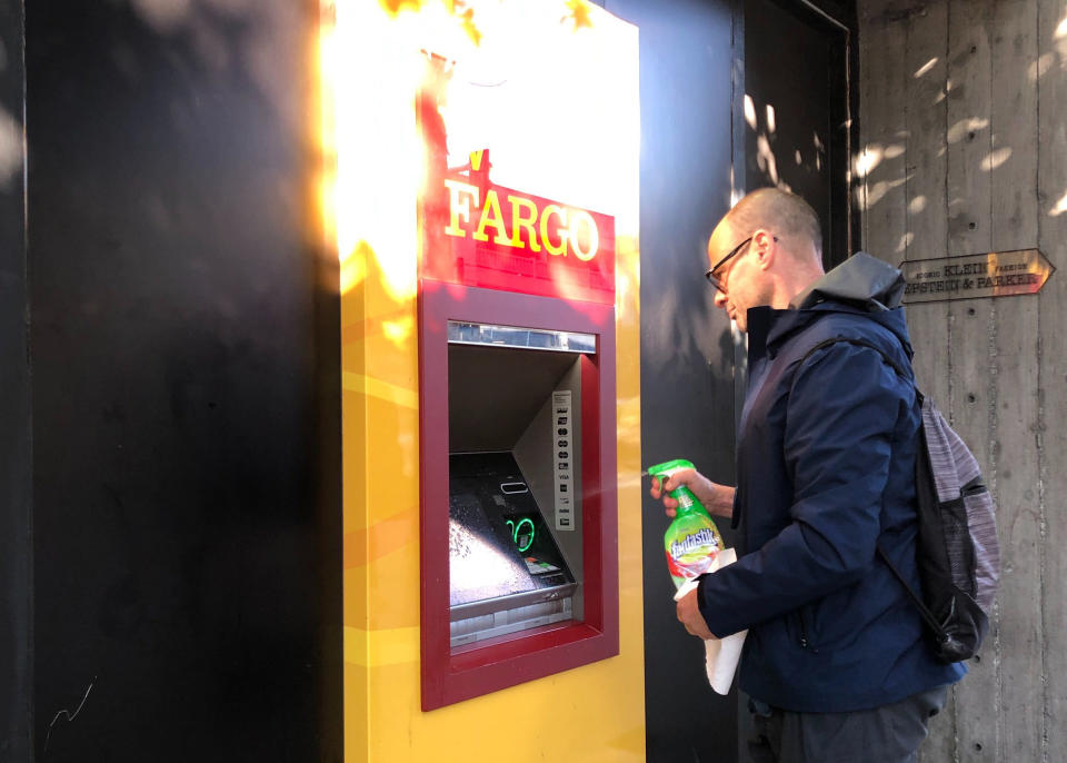 David Mayer, a personal trainer and yoga instructor in San Francisco, sprays down a Wells Fargo ATM machine before using it in San Francisco on Friday, March 20, 2020. Nearly 40 million people in California awoke Friday to the reality of a near lockdown to prevent the spread of coronavirus. (AP Photo/Olga R. Rodriguez)