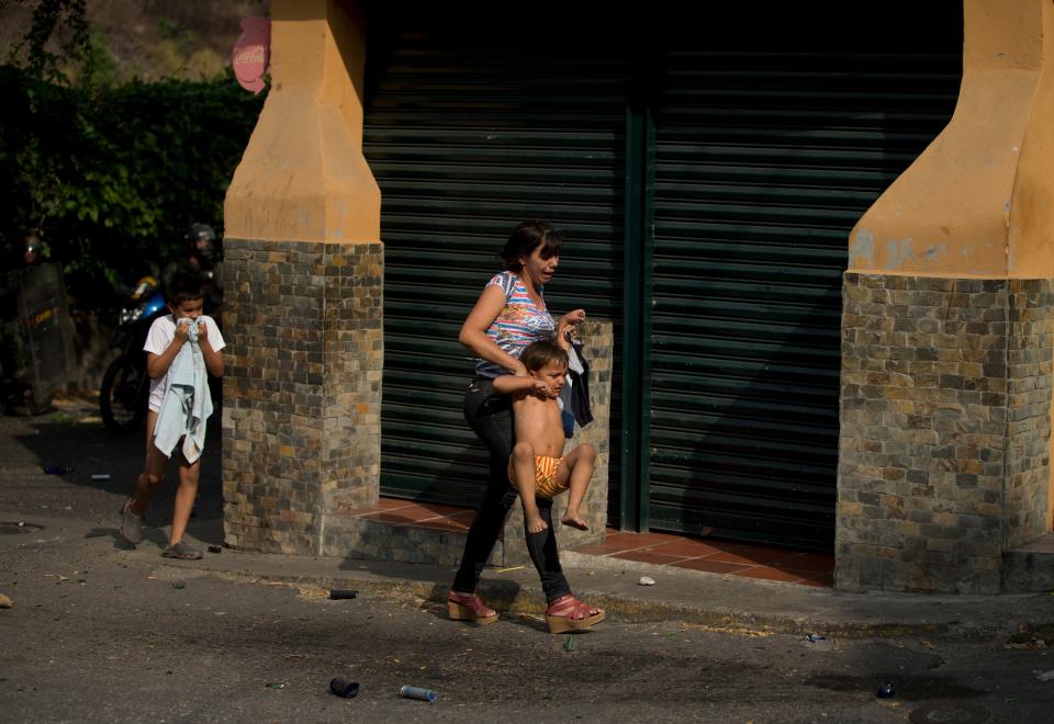 A woman and her sons take cover from the tears gas fired by Bolivarian National Guards soldiers toward demonstrators during clashes at an anti-government protest in Caracas, Venezuela, Saturday, April 26, 2014. Student organizers at the last minute decided against marching downtown to avoid a confrontation with security forces in the government-controlled district. Instead they concentrated in the wealthier, eastern neighborhoods that have been the hotbed of unrest since February. (AP Photo/Fernando Llano)