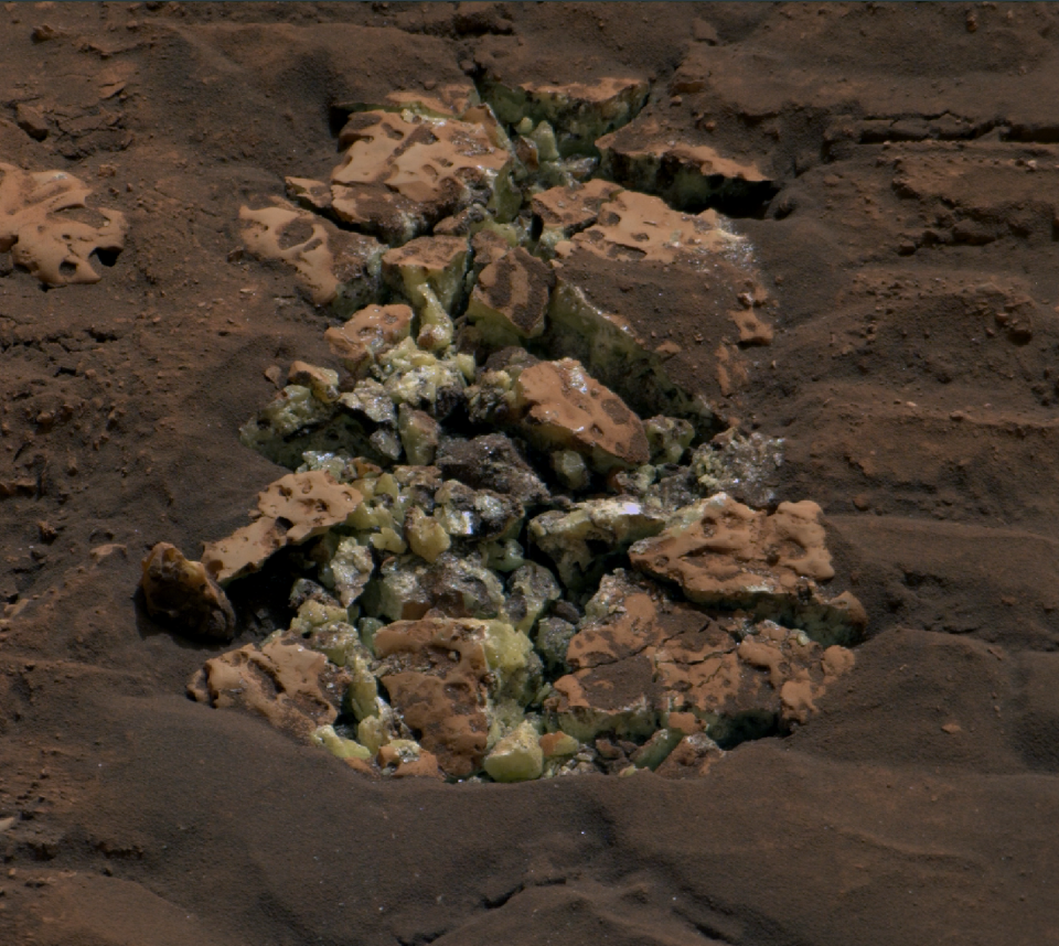 Uma rocha atropelada e quebrada pelo rover Curiosity revelando cristais amarelos de enxofre