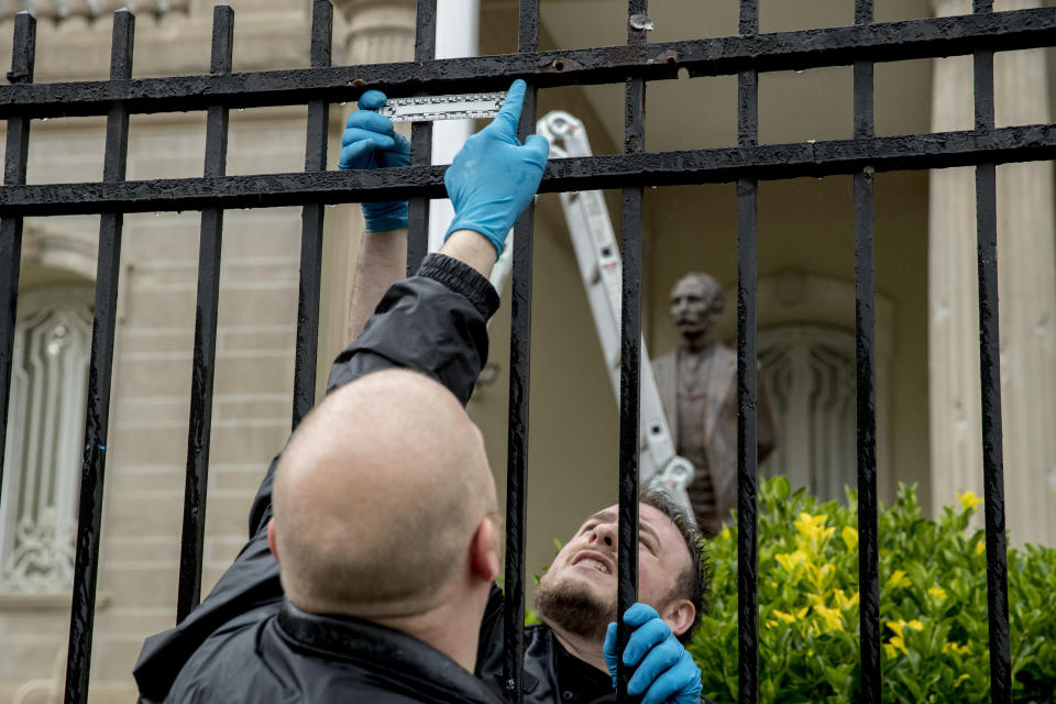 A statue of Cuban national hero Jose Marti is visible behind Secret Service investigators as they look at bullet holes in a fence after police say a person with an assault rifle opened fire at the Cuban Embassy, Thursday, April 30, 2020, in Washington. (AP Photo/Andrew Harnik)