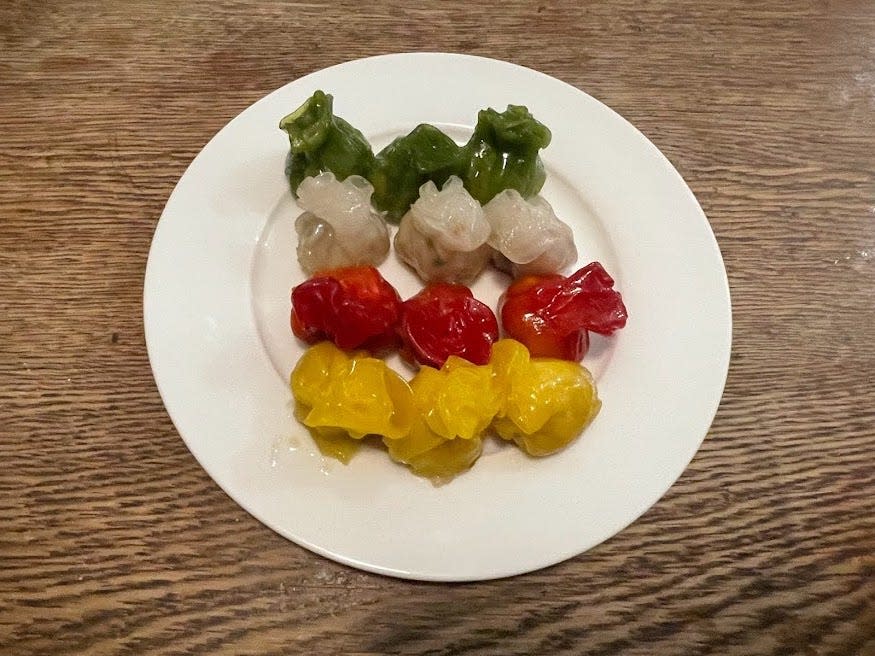 Three each of green, white, red, and yellow shrimp pouches on white a plate placed on a wooden counter