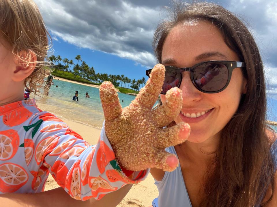 A woman taking a selfie with a partially pictured child who has a sandy hand.