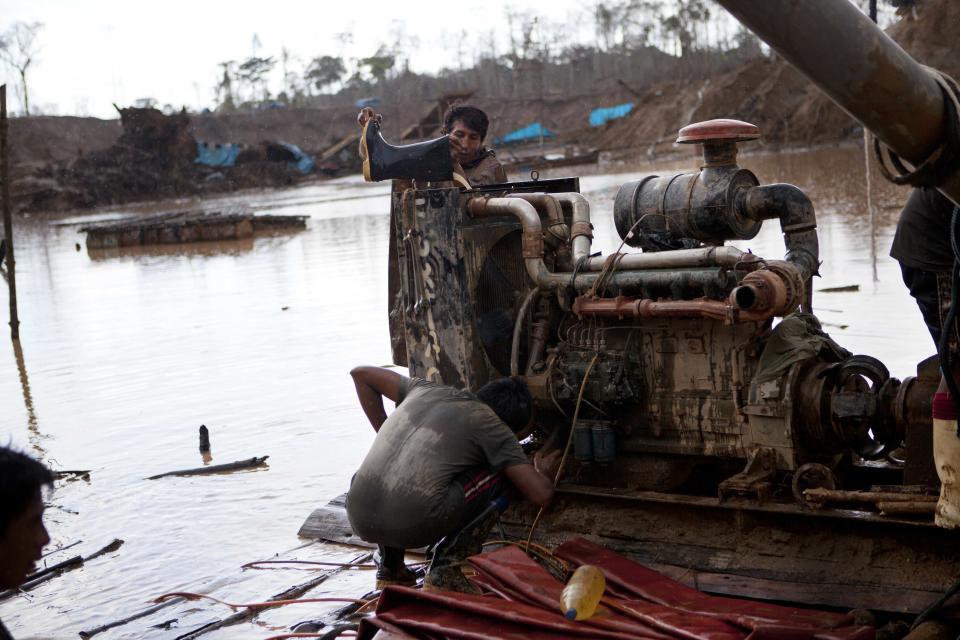 In this May 4, 2014 photo, a miner uses a boot to fill with water the radiator of a rustic type of hydraulic jet known locally as a "Chupadera," used to to mine for gold at a gold mine process in La Pampa in Peru's Madre de Dios region. Miners sweat through 28-hour shifts in the malarial jungle of the Madre de Dios region in southeaster Peru, enduring for a few grams of gold the perils of collapsing earth and limb-crushing machinery. (AP Photo/Rodrigo Abd)