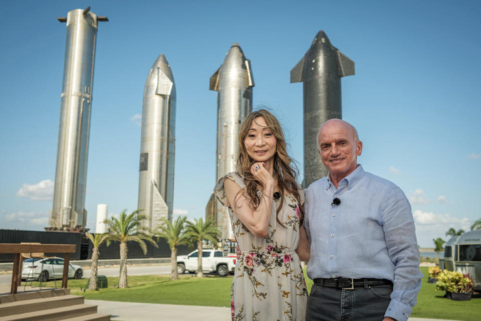 Akiko and Dennis Tito at SpaceX's Starbase flight test facility on the Gulf Coast near Boca Chica, Texas. The Super Heavy first stage booster is visible at left, along with three versions of the Starship upper stage designed to carry passengers and payloads to the moon and beyond. / Credit: CBS News