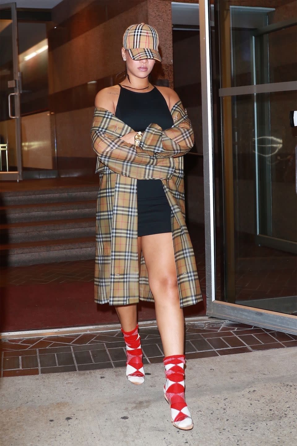 <p>In a Burberry hat, trench coat, and argyle socks, clear heels, black minidress, and gold watch while out in New York.</p>