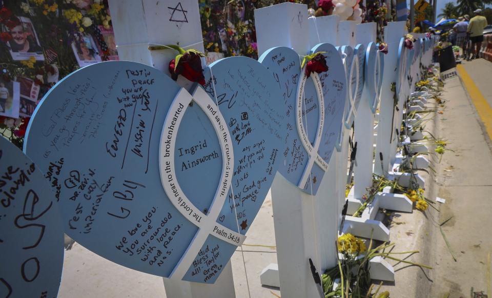 FILE - In this July 11, 2021, file photo, wooden hearts with the names of victims are erected along side the photos, flowers, and other memorial items as visitors walk through the memorial site for the Champlain Towers South condo building collapse in Surfside, Fla. A judge pushed on Wednesday, Oct. 20, 2021, for compromise on potential payouts between people who lost loved ones and those whose units were destroyed in the deadly collapse of a Florida beachfront condominium. (Carl Juste/Miami Herald via AP, File)