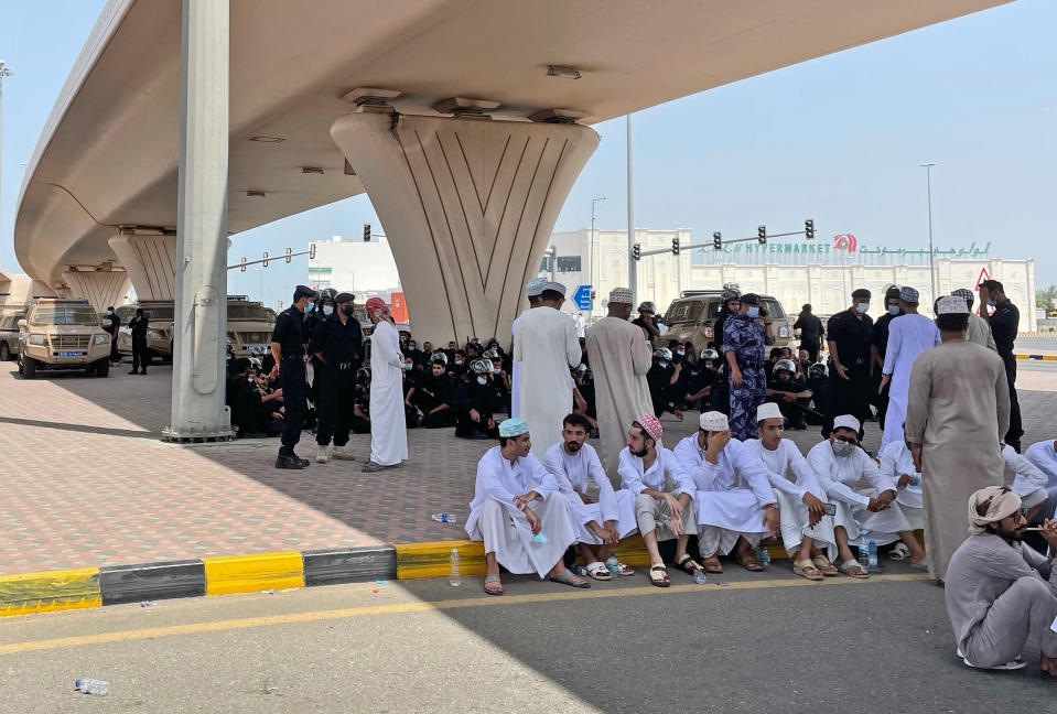 People and security forces talk under a bridge, in Sohar, Oman, Tuesday, May 25, 2021. On Tuesday, dozens of protesters angry over firings and the poor economy of Oman marched in Sohar, a city some 200 kilometers northwest of the capital, marking a third day of demonstrations in the typically subdued sultanate. (AP Photo)