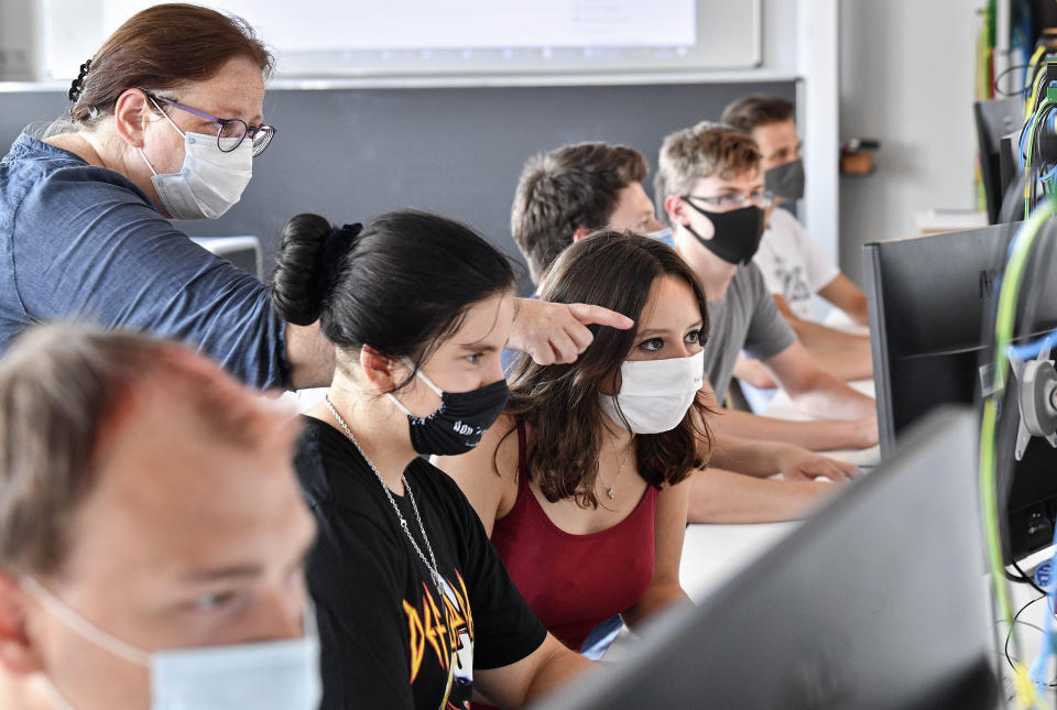 FILE - In this Thursday, Aug. 13, 2020 file photo students of the Robert-Koch vocational college get advise by their teacher, wearing face masks in the classroom, during computer science lessons in Dortmund, Germany. The German government on Wednesday agreed on a strategy to boost the use of data for commercial purposes and signed a deal with state education authorities to fund laptops for teachers who have to work from home because of the virus lockdown. (AP Photo/Martin Meissner, file)