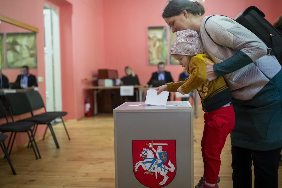 A woman with a child casts a ballot at a polling station during the first round of voting in presidential elections in Vilnius, Lithuania, Sunday, May 12, 2024. (AP Photo/Mindaugas Kulbis)