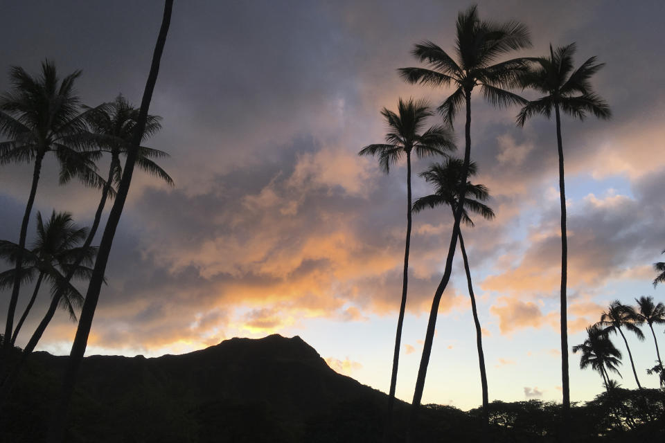 The sun rises behind the Diamond Head State Monument in Honolulu, on Jan. 16, 2018. Taking care of Hawaii's unique natural environment costs money and now the state wants tourists to help pay for it, especially because growing numbers are traveling to the islands to enjoy the beauty of its outdoors — including some lured by dramatic vistas they've seen on social media. (AP Photo/Eric Risberg)