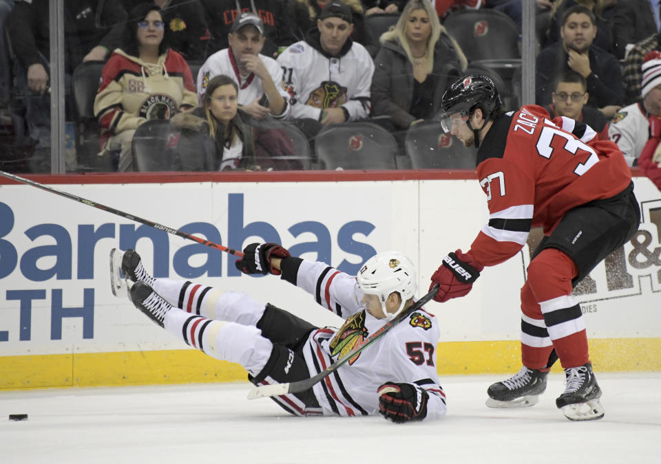 Chicago Blackhawks left wing Anton Wedin (57) hits the ice as he chases after the puck with New Jersey Devils center Pavel Zacha (37) during the first period of an NHL hockey game Friday, Dec. 6, 2019, in Newark, N.J. (AP Photo/Bill Kostroun)