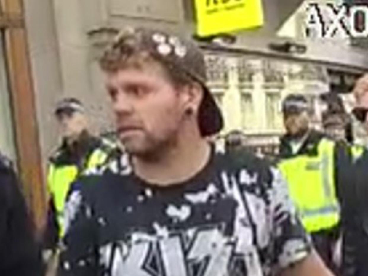 The man can be seen wearing a back-to-front peaked cap, dark shorts and a black and white T-shirt with the logo of the band Kiss on the front: Met Police