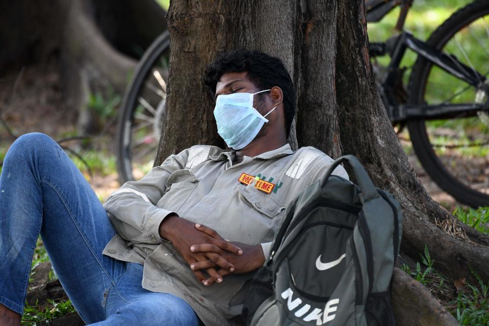 A man wearing a face mask, as a preventive measure against the spread of the COVID-19 coronavirus, and a tag that reads "Safety starts with me,| takes a nap while waiting for transport to work in Singapore on April 15, 2020. - Singapore won praise for keeping its outbreak in check in the early stages of the fight against the COVID-19 novel coronavirus but has seen a surge in cases this month, with many linked to foreign workers' dormitories. (Photo by ROSLAN RAHMAN / AFP) (Photo by ROSLAN RAHMAN/AFP via Getty Images)