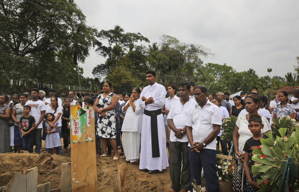 Sri Lankan Roman Catholic priests Father Anthony Nishan participates in a funeral service of a victim of Easter Sunday's church explosion of Katuwapitiya in Colombo, Sri Lanka, Thursday, April 25, 2019. There are 41 dirt mounds piled with flowers and candles, with wooden crosses marked mostly with numbers that correspond to names in a book that the priests keep. There's fear of more violence and deep grief in this majority Christian enclave outside Colombo. "The whole village is a funeral. The houses here are filled with coffins," Nishan said of a place where about 120 Christians died in the bombing. (AP Photo/Manish Swarup)