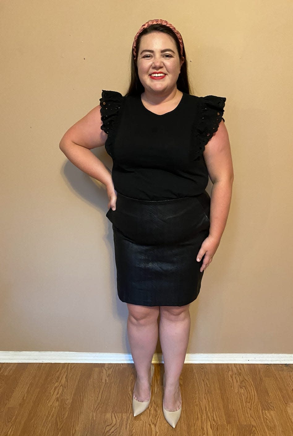 The writer wearing a black top with flutter sleeves and a leather skirt and nude pointde heels