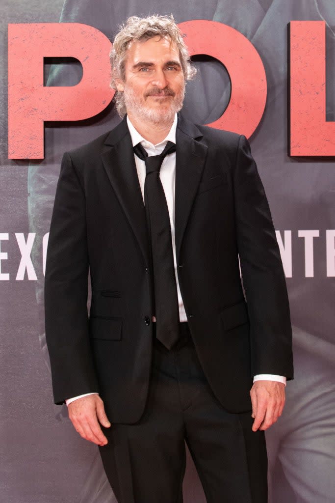 Joaquin in a suit and tie stands in front of a backdrop with text, at an event