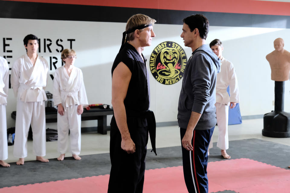 William Zabka and Ralph Macchio facing off with karate students behind them in a scene from "Cobra Kai"