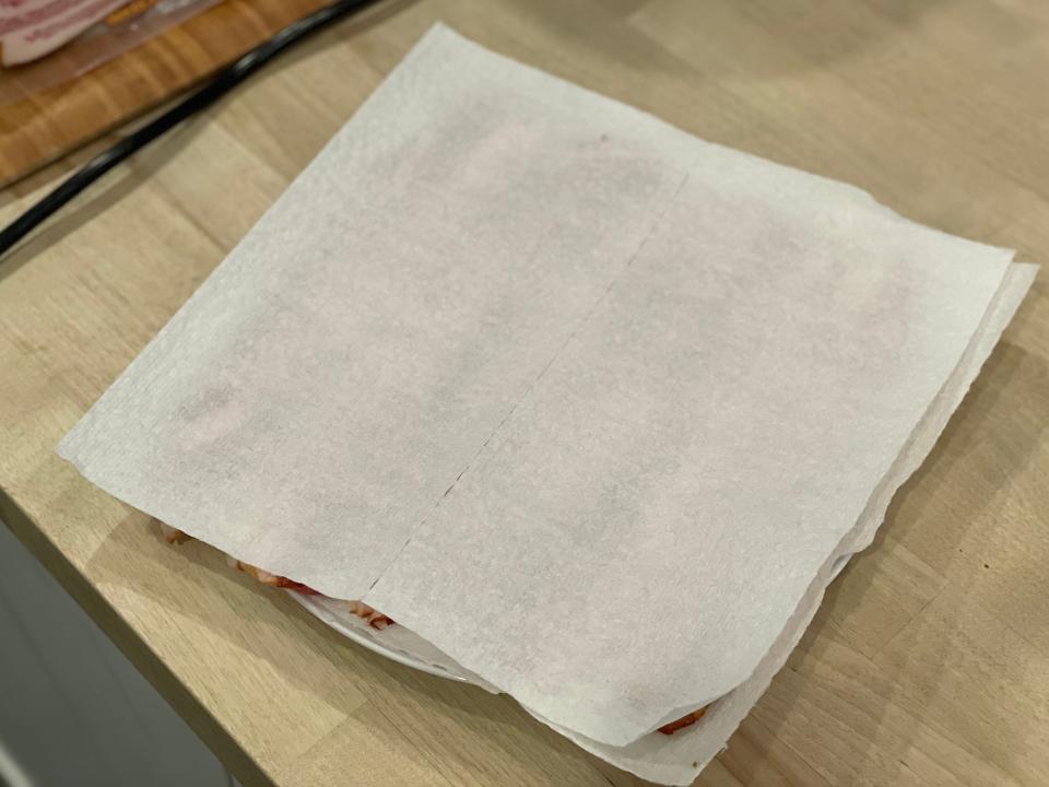 sheet of paper towel over bacon strips on a plate