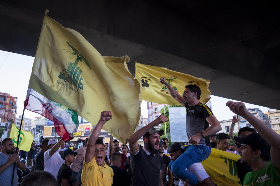 FILE - In this June 28, 2020 file photo, Hezbollah and Amal supporters wave Hezbollah and Iranian flags as they shout slogans against Israel and U.S. during a protest in the southern suburb of Beirut, Lebanon. For many, the Iran-backed Hezbollah now stands at the top of Lebanon’s sectarian-based system of power — and so is complicit in the corruption many blame for the port disaster and for driving the country into near bankruptcy. (AP Photo/Hassan Ammar, File)