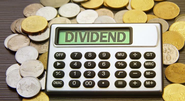 dividend stocks: A calculator projecting the word "DIVIDEND" rests on a pile of gold and silver coins.