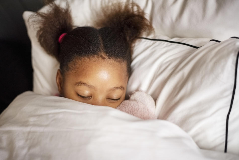 A young girl lays in bed with her eyes closed.