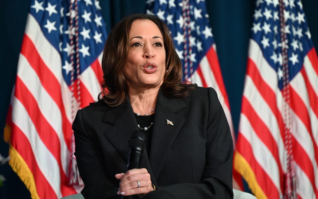 Kamala Harris holds a microphone in front of a row of US flags