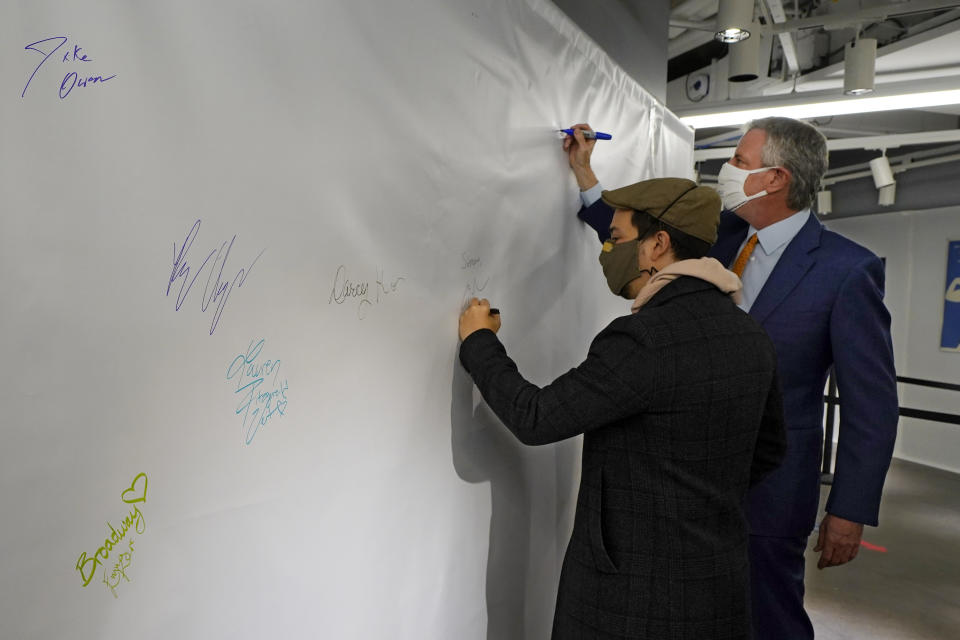 Actor Lin-Manuel Miranda, left, and New York Mayor Bill de Blasio, sign the autograph wall after they toured the grand opening of a Broadway COVID-19 vaccination site intended to jump-start the city's entertainment industry, in New York, Monday, April 12, 2021. (AP Photo/Richard Drew, Pool)