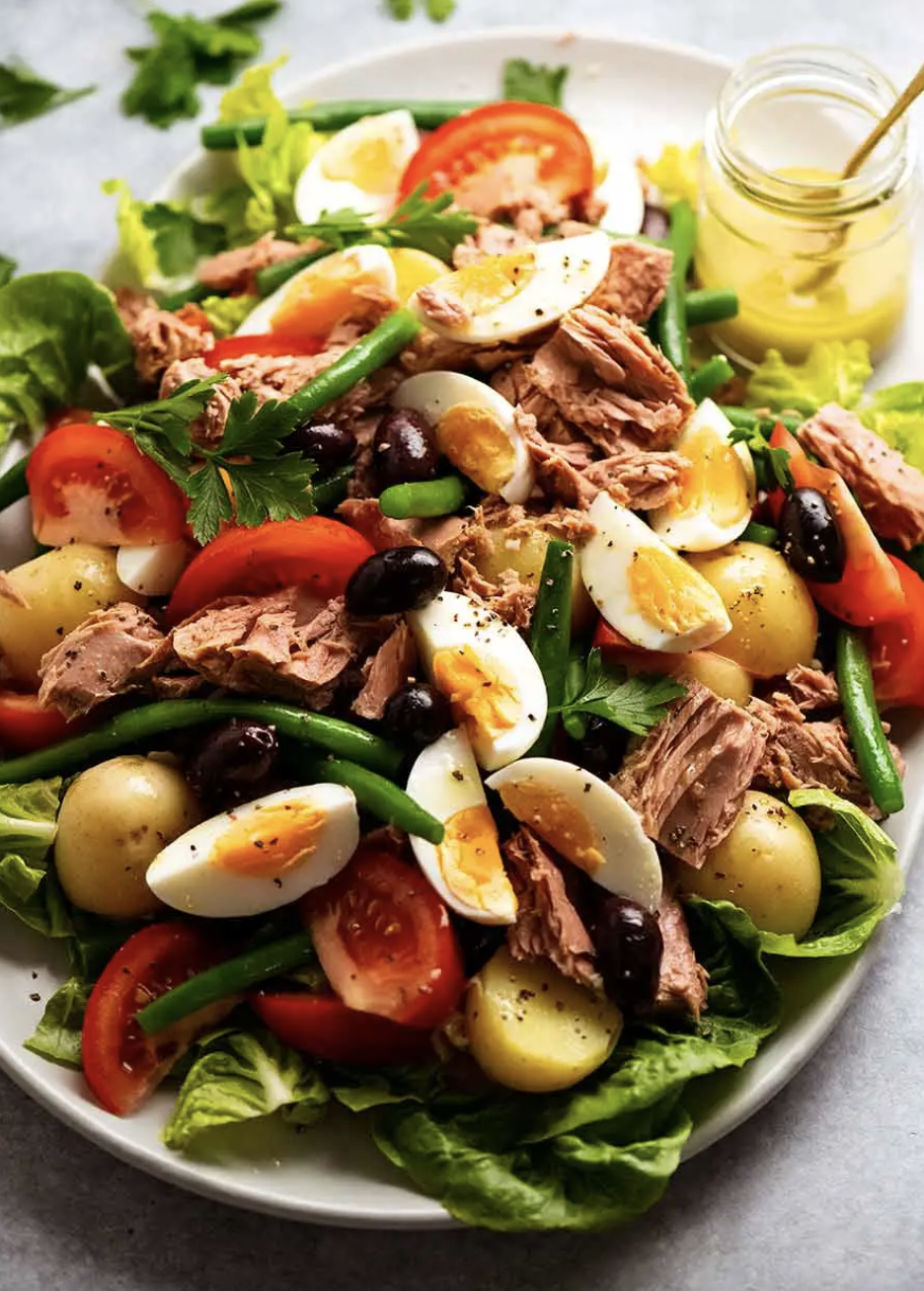 A plate of Nicoise salad with tuna, eggs, tomatoes, green beans, potatoes, and olives