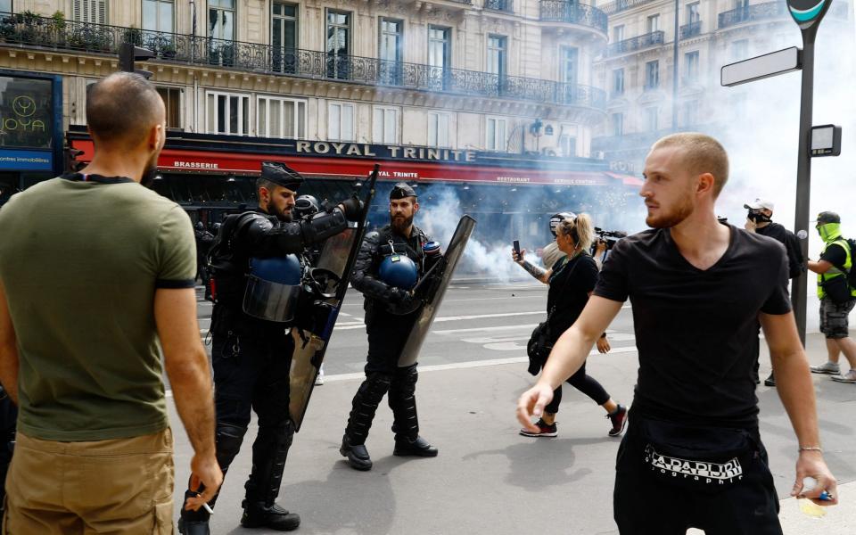 Protesters and riot police stand amidst tear gas smoke during clashes on the sidelines of a demonstration - Sameer Al-DOUMY / AFP