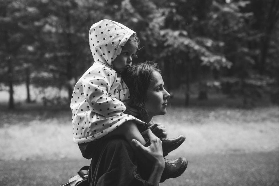 Child in a hooded polka-dot top sits on an adult's shoulders, both looking away contemplatively