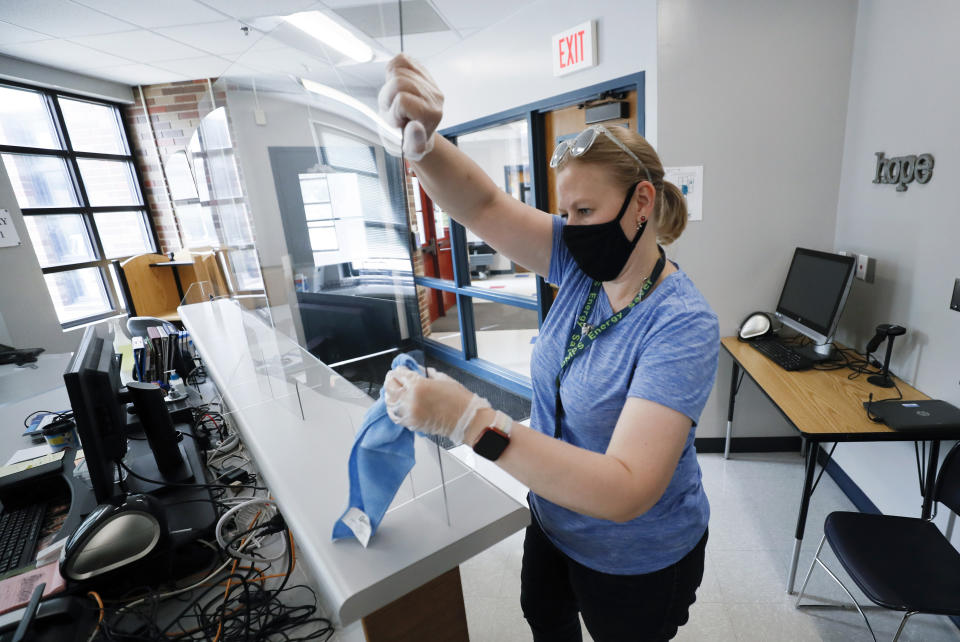 Des Moines Public Schools Admin Support Coordinator Sarah Holland installs a plexiglass shield in the office at Oak Park Elementary School, Thursday, July 30, 2020, in Des Moines, Iowa. (AP Photo/Charlie Neibergall)