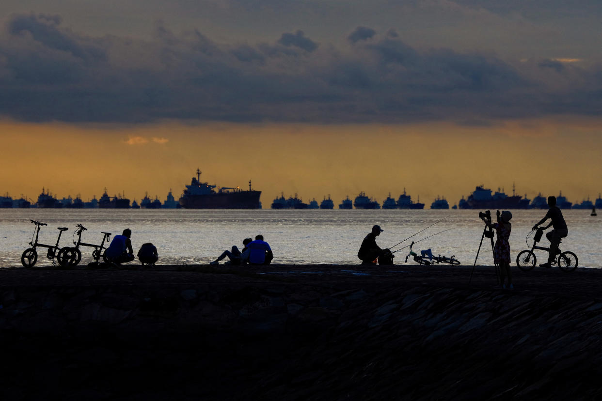 People are silhouetted at sunrise along with vessels anchored along the southern coast on May 30, 2021 in Singapore. Singapore enters a month long heightened alert from May 16 to June 13 to curb the spread of COVID-19 cases in the local community. New restrictions on movements and activities have been introduced such as limiting social interaction to two, prohibiting dining out and a reduced operating capacity at shopping malls, offices and attractions. (Photo by Suhaimi Abdullah/NurPhoto via Getty Images)