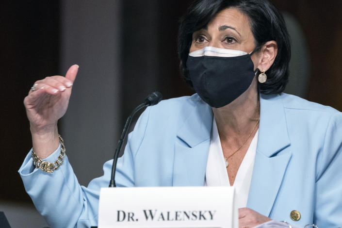 Dr. Rochelle Walensky speaks into a microphone while wearing a face mask in front of a placard bearing her name.
