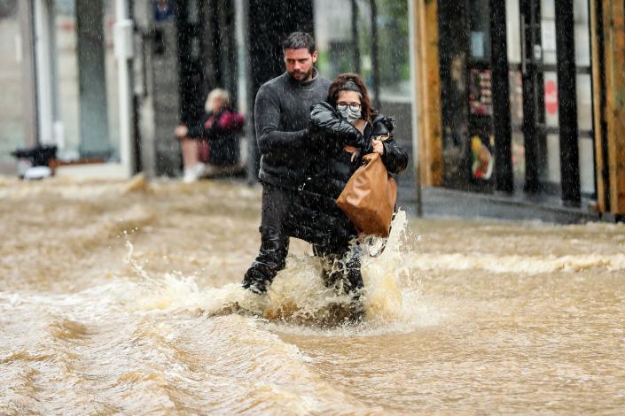 A man helps a woman navigate a flooded street in downtown Spa, Belgium, Thursday