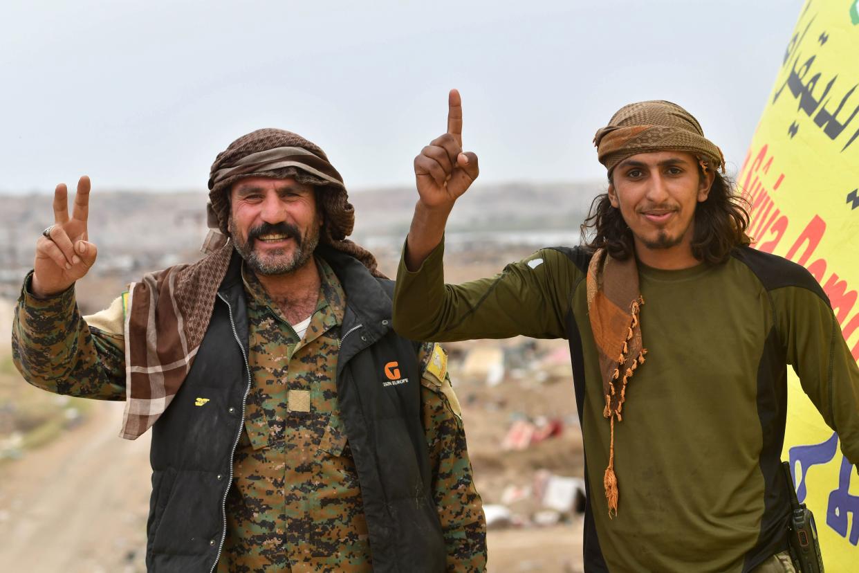 Members of the Syrian Democratic Forces flash gestures with their hands while standing next to the SDF’s unfurled flag while on watch duty in the village of Baghouz in Syria (Picture: AFP/Getty)