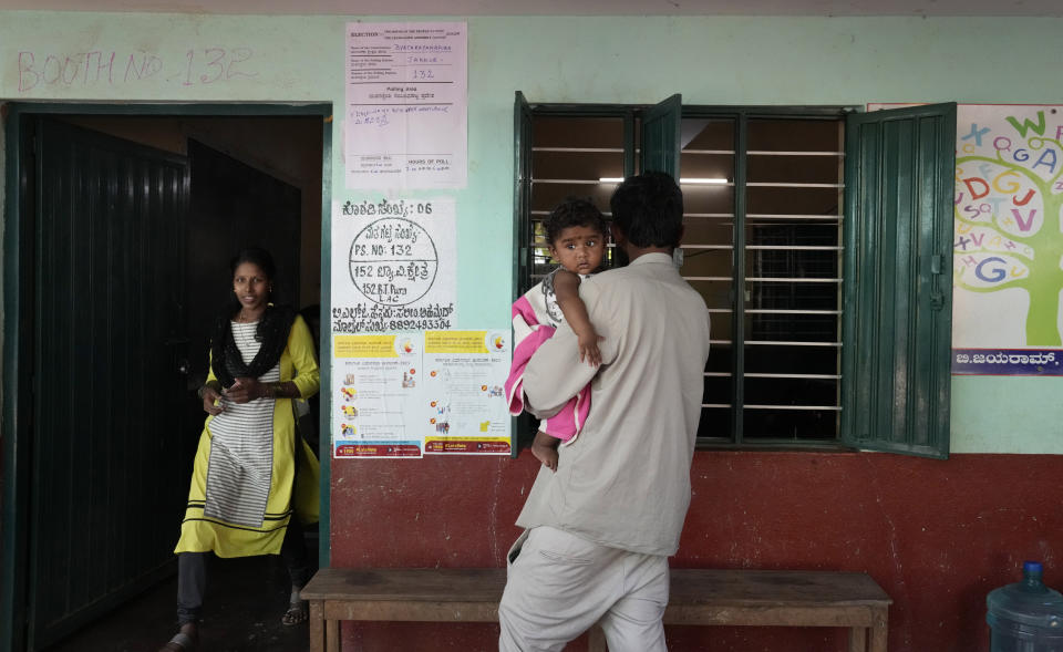 A woman comes out from a polling booth after casting her vote as her husband waits with their child, in Bengaluru, India, Wednesday, May 10, 2023. Thousands of people began voting Wednesday in a key southern Indian state where pre-poll projections have put the opposition Congress ahead of Prime Minister Narendra Modi's governing Hindu nationalist party. (AP Photo/Aijaz Rahi)